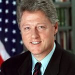 Portret van Bill Clinton in donkerblauw pak, glimlachend, formele setting.