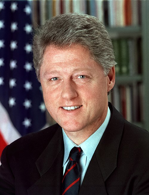 Portret van Bill Clinton in donkerblauw pak, glimlachend, formele setting.