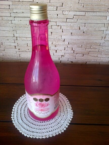 Rozenwater sprayfles met rozenblaadjes in heldere vloeistof.