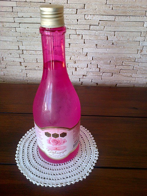 Rozenwater sprayfles met rozenblaadjes in heldere vloeistof.