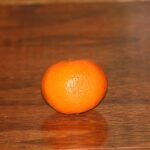 Rijpe clementine op houten tafel, met groen blad en schil.