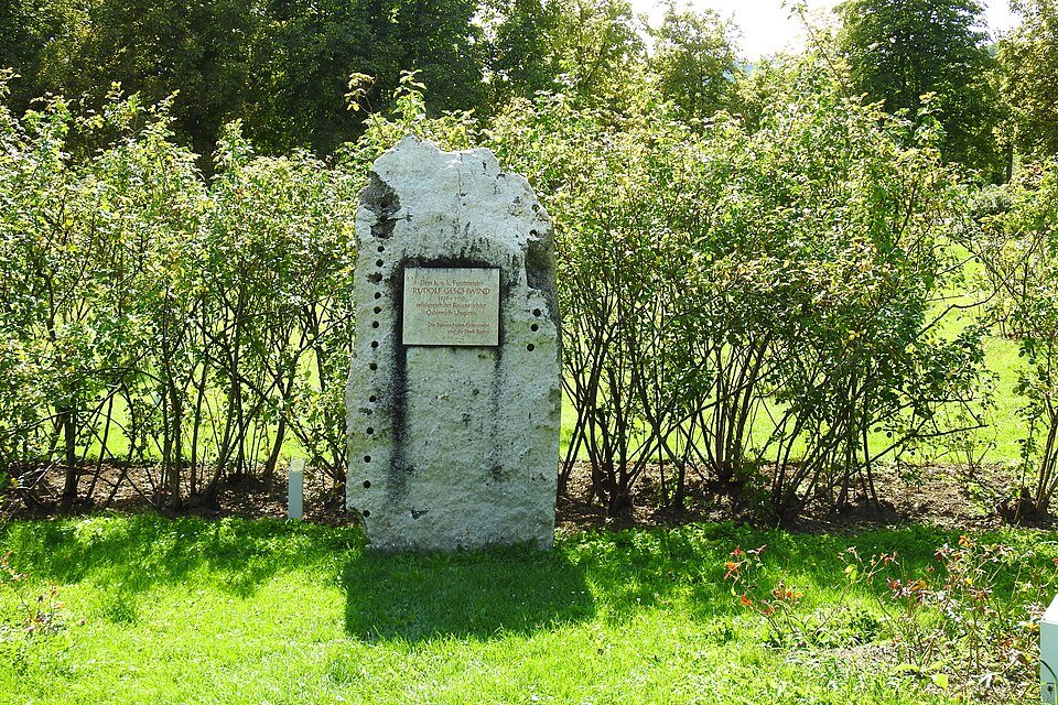 Gedenksteen voor Rudolf Geschwind in schaduwrijke setting.