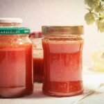 Hagebuttenmarmelade in glazen pot met rode bessen op houten tafel.