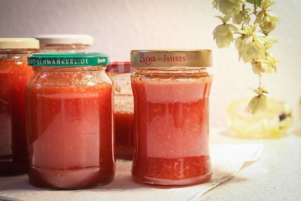 Hagebuttenmarmelade in glazen pot met rode bessen op houten tafel.